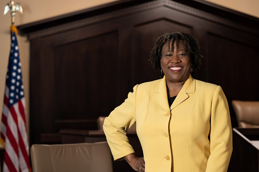 woman in a yellow suit crossing her arms in front of a judge's bench
