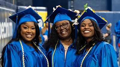 Three female SPC graduates wearing their caps and gowns smiling at their graduation ceremony