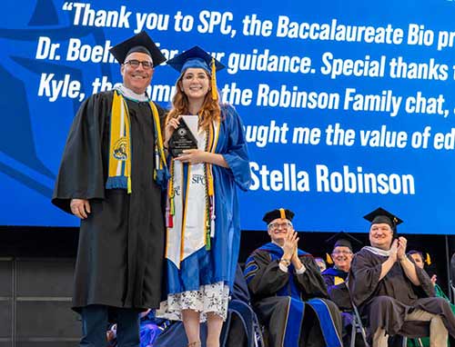 SPC graduate Stella Robinson posing in her blue cap and gown with Jesse Turtle
