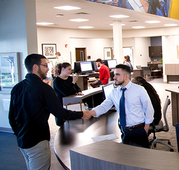 academic advisor in a white shirt and tie shaking hands with a make student in a black shirt