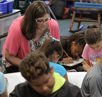 teacher in a pink sweater working with elementary students