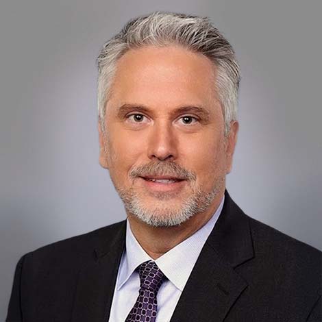 A portrait of Dr. Brian Lucas wearing a black suit coat over a white dress shirt and a black and white tie.
