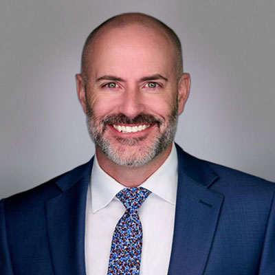 Portrait of Jason Butts wearing a blue suit coat, white dress shirt and a blue and white tie.