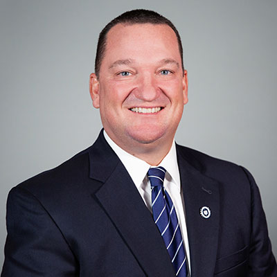 Portrait of Thomas Kidwell, wearing a blue suit coat, white dress shirt, and blue and white tie.