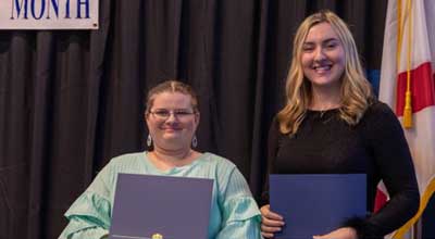 2 conference attendees holding blue folders and smiling