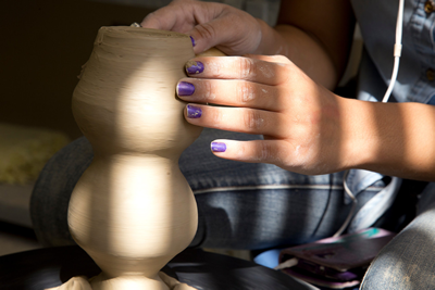 pair of hands shaping clay on a potter wheel