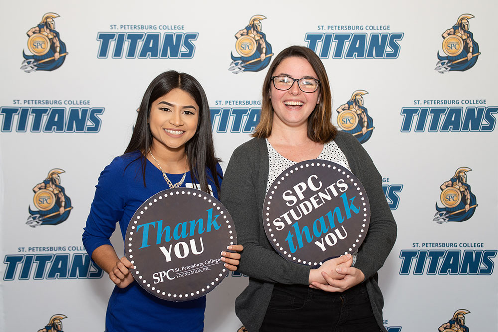 two female students smiling holding thank you cards in front of a blue and white SPC Titans background