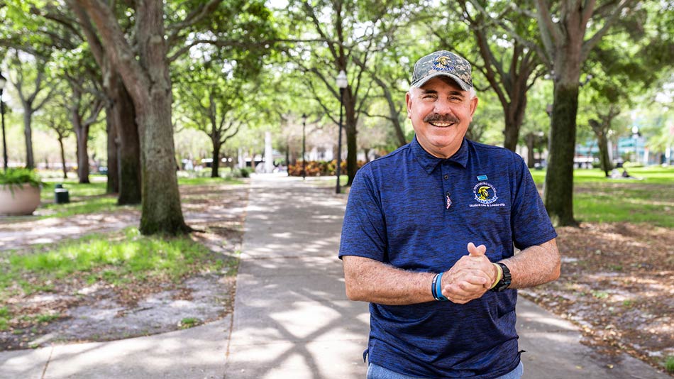 older male veteran wearing a camo baseball cap and a blue SPC polo shirt