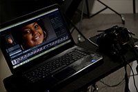 the face of a woman on a laptop screen next to a SLR camera