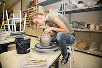 female student working with clay on a pottery wheel