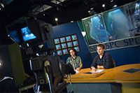 male and female students sitting at a broadcast desk in a tv studio