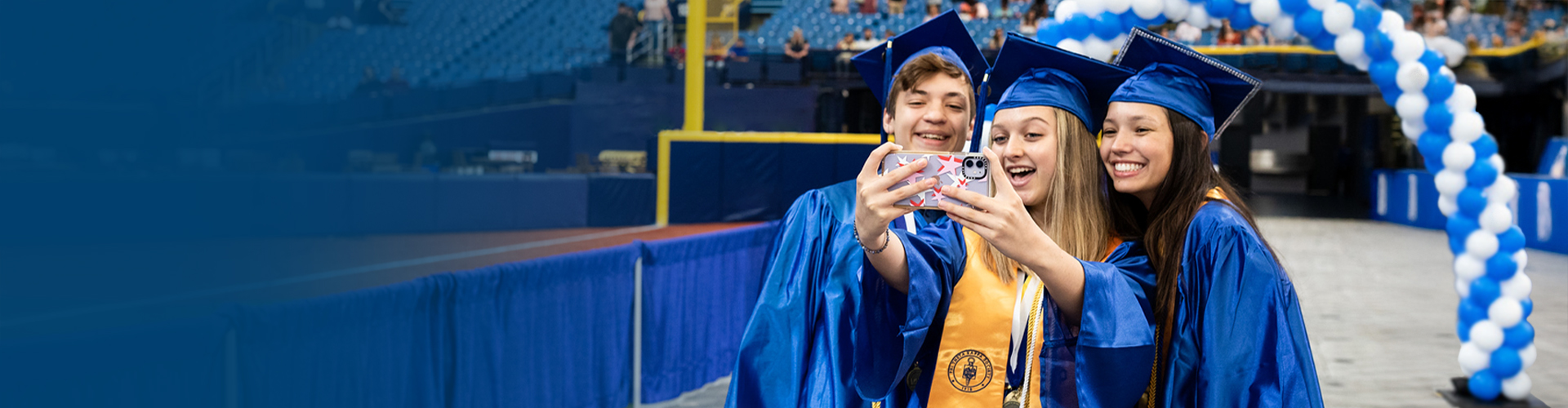 Collegiate high school students taking a selfie at graduation with their caps and gowns on