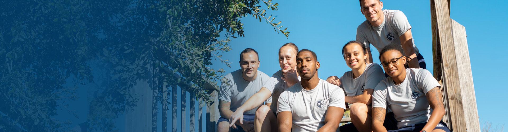 blue gradient image fading into a group of law enforcement academy recuits dressed work out gear in front of an obstacle course